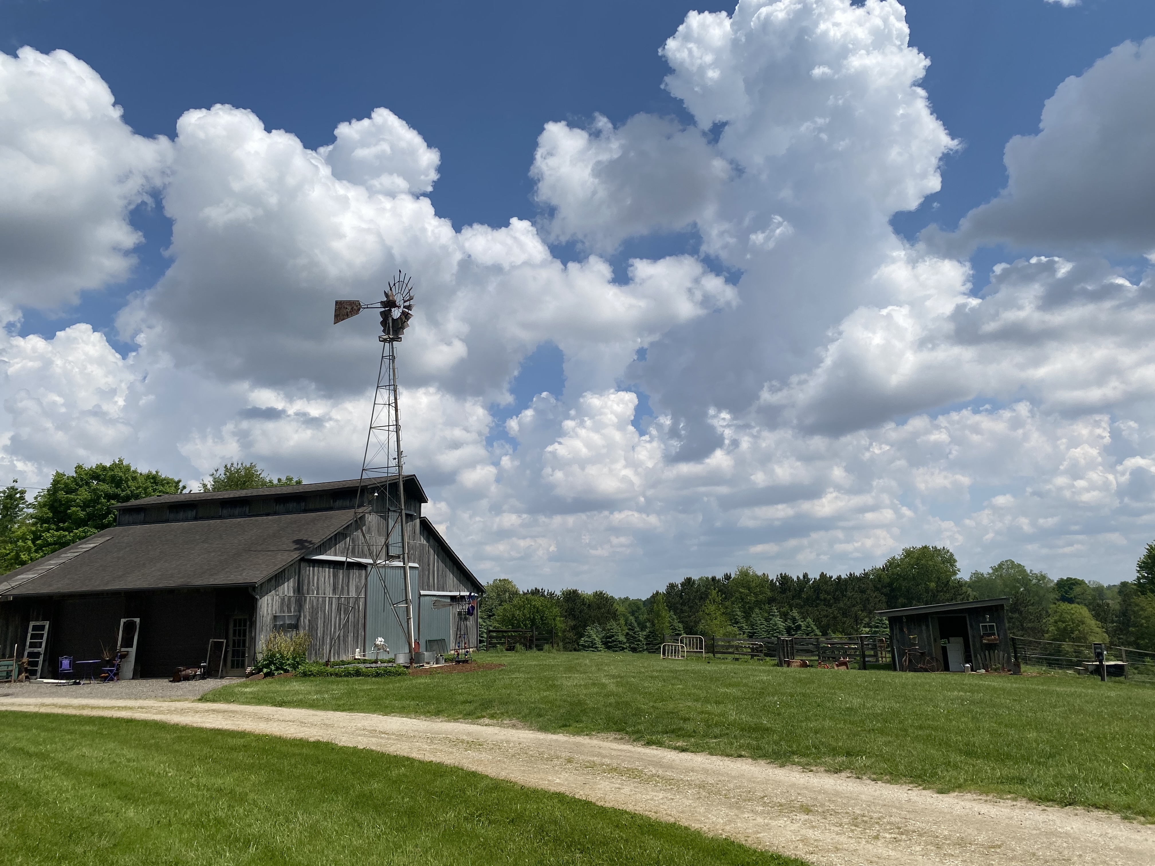 Large wood barn and windmill located at a farm with blue sky and white fluffy clouds